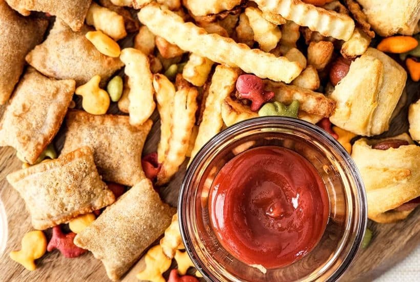 Image of finished charcuterie board arranged on a wooden board with condiments in glass dish